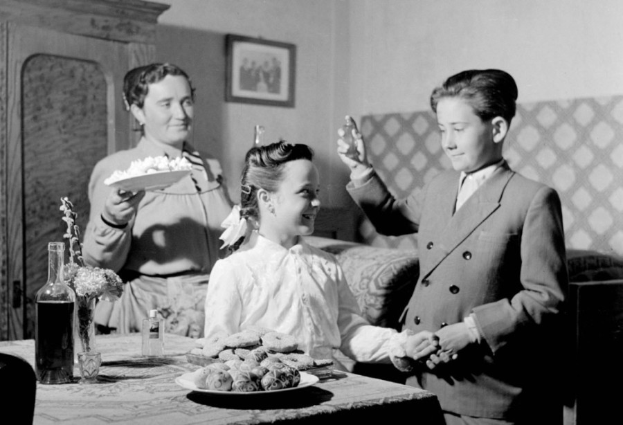 Miske, 1955.04.10. Az első locsoló Kiss János kölnis üvegből meglocsolja Király Ilonkát, Király Péterné hímes tojással és süteménnyel kínálja a fiút. (Fotó: MTI Fotó / Magyar Fotó: Tormai Andor)